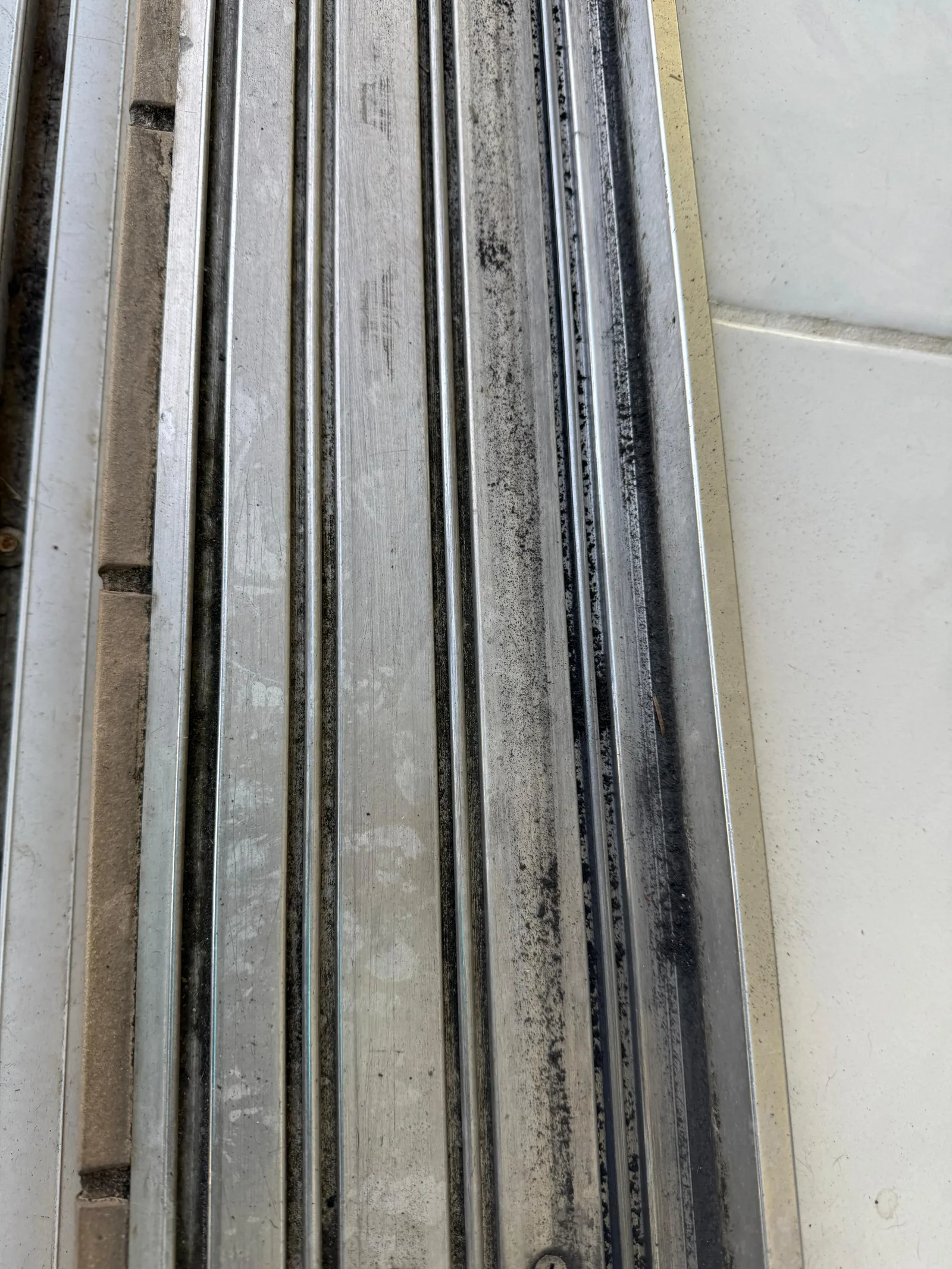 Dirt and debris packed inside a sliding door bottom track, blocking the rollers